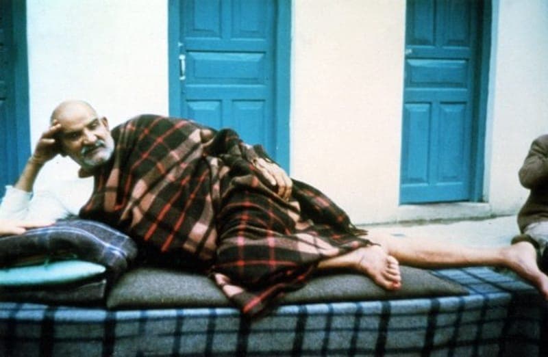 Neem Karoli Baba reclining on a bench beside blue doors
