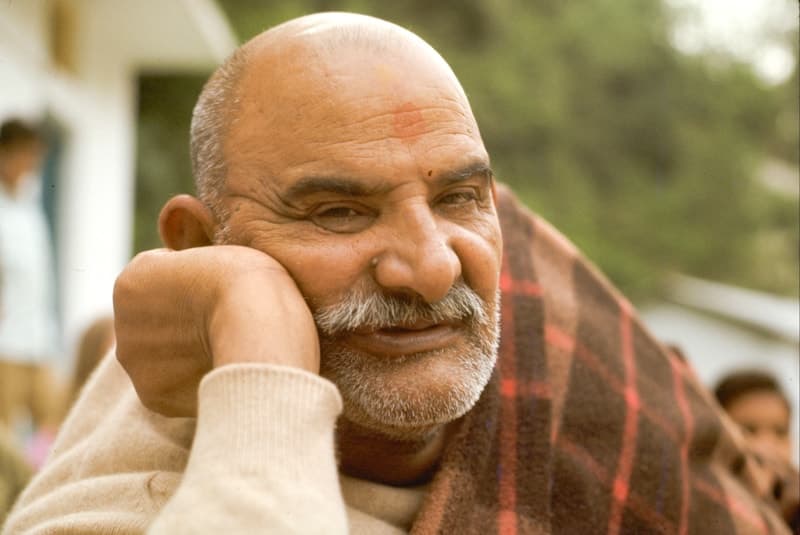 Neem Karoli Baba resting his chin on his hand, wrapped in a red plaid blanket
