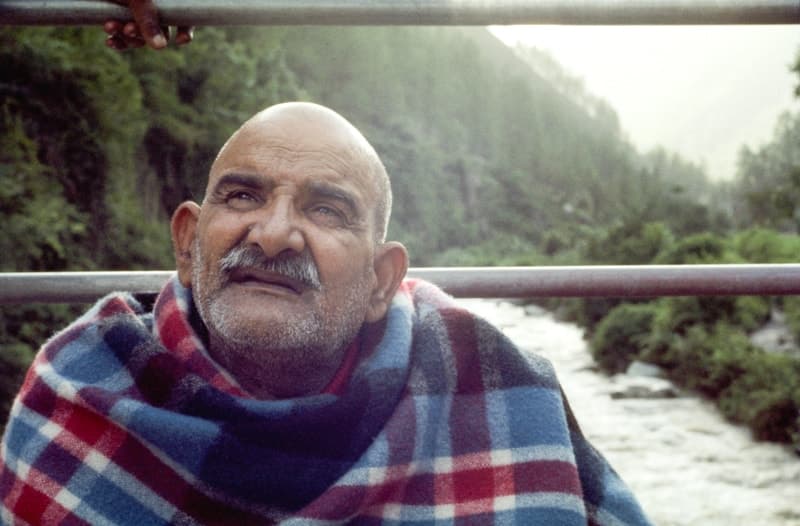 Neem Karoli Baba wrapped in a plaid blanket above a river valley in the Himalayan foothills