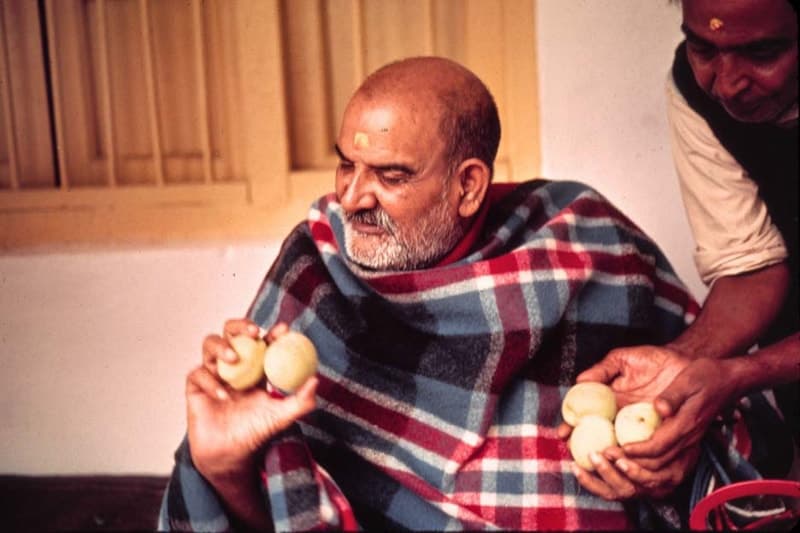 Neem Karoli Baba holding green apples as a devotee hands him more