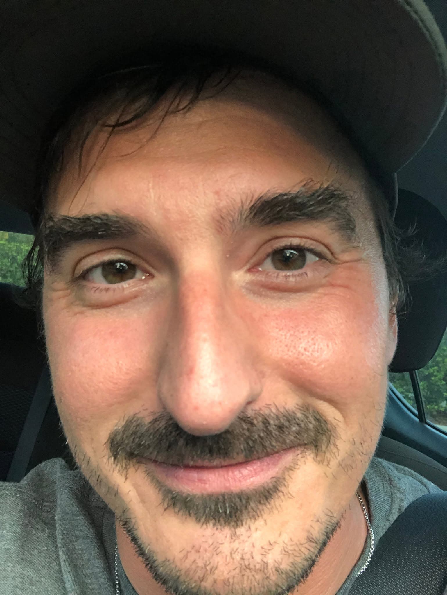 Tom smiling in a dark cap while sitting in a car