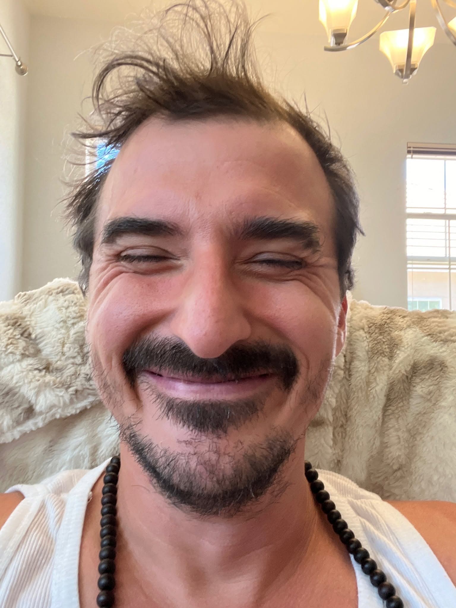 Tom smiling at home in a white tank top and black prayer beads