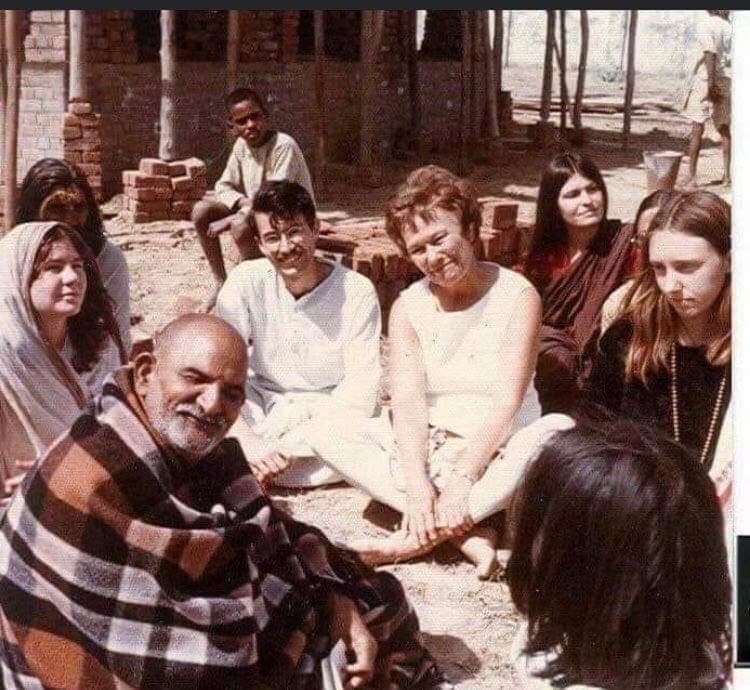 A bearded man wrapped in a plaid blanket sitting outdoors with a group of people.