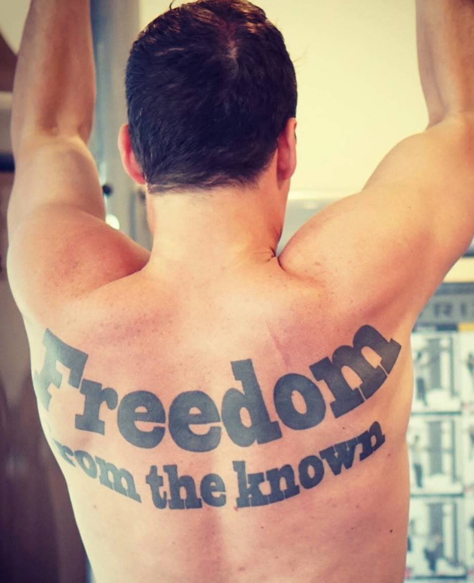 Thomas Whigham's bare back with arms raised, tattooed with the words "Freedom from the known."