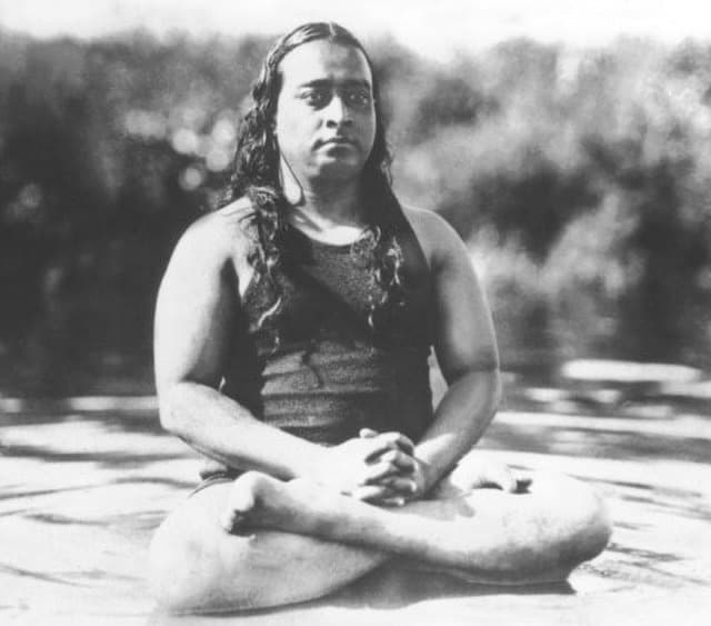 Black-and-white portrait of a long-haired man in a dark robe sitting cross-legged in meditation outdoors.