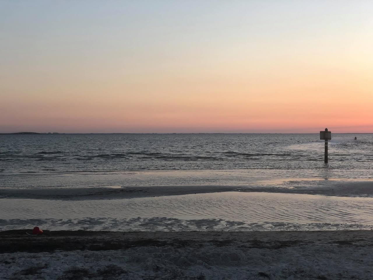 Fading sunset light over a quiet shoreline, with a channel marker in the water on the right.