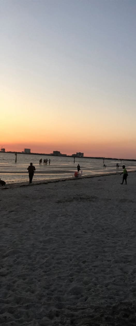 Tall view of a beach at sunset with a few people walking in silhouette along the sand.