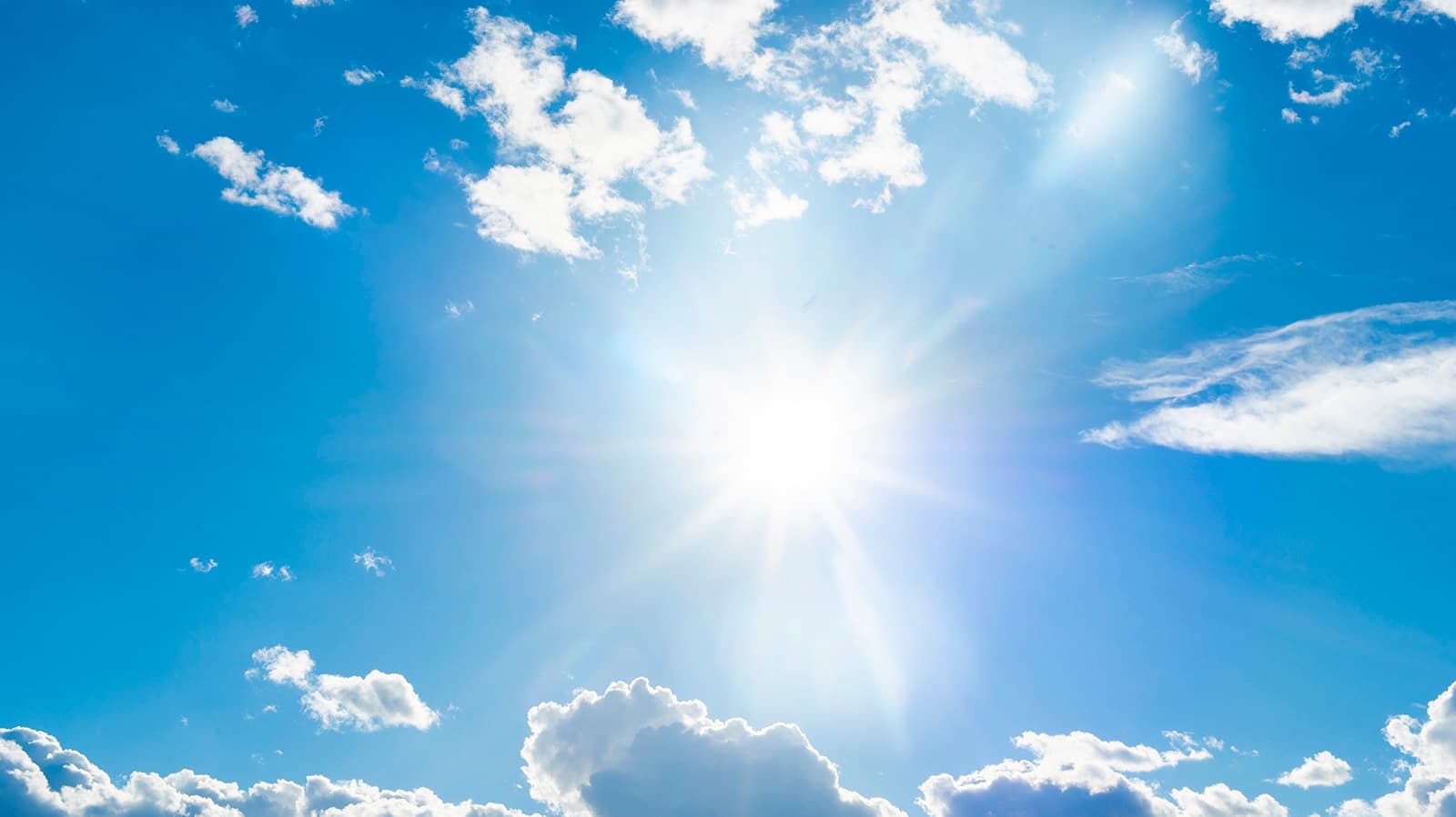 The sun blazes in a bright blue sky scattered with white clouds.